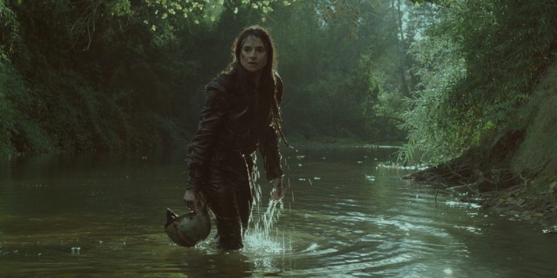 A still from A Cow Who Sang a Song Into the Future, one of the best 2022 queer festival movies. A woman emerges from a lush green river holding a motorcycle helmet.