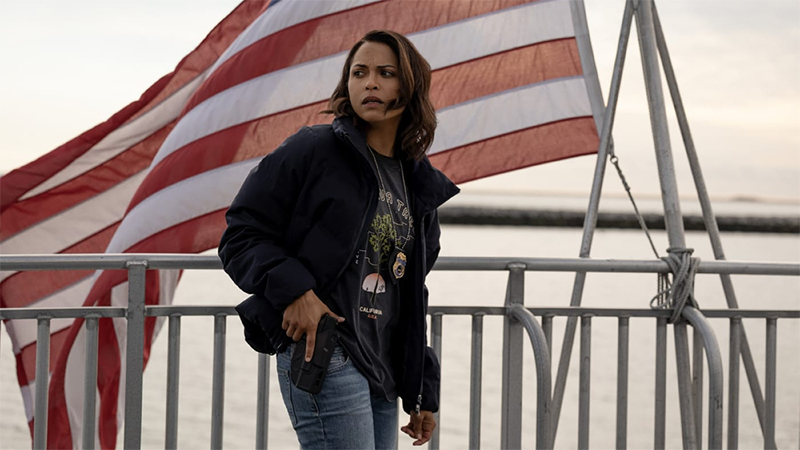 Jackie stands in front of an American flag with her hand on her gun