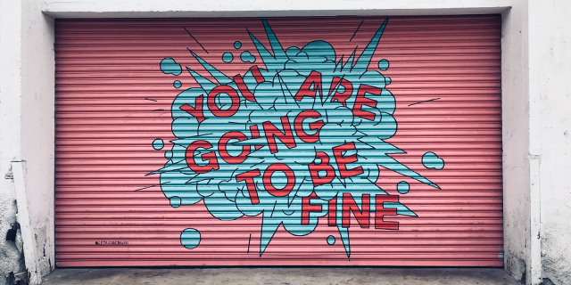 The words "You are going to be fine" written on a garage style door that is painted a soft pink.