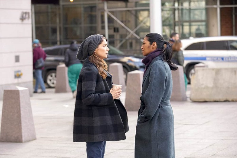 Outside in the cold New York winters, Leyla confronts Lauren about her decision to leave New Amsterdam. Both are wearing winter coats. Lauren has a slouchy grey beanie and is holding a coffee.