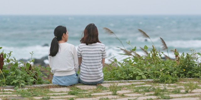 Two women sitting shoulder to shoulder looking at the ocean