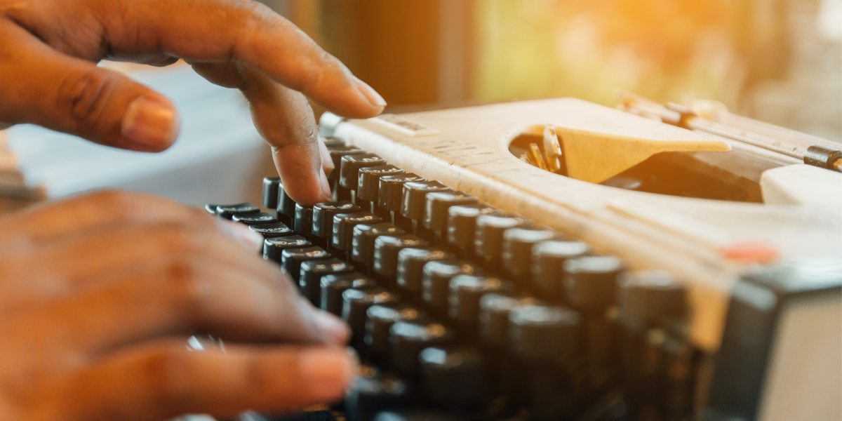 A person with brown skin types on a typewriter.