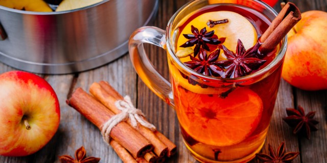 A mug with apple cider and star anise in it next to a bunch of cinnamon sticks tied together with twine for the winter mocktails recipe list