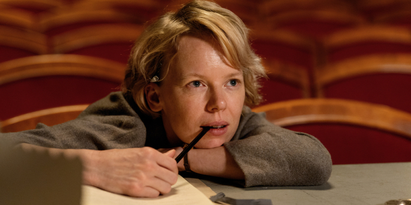 Alma Poystï leans her arms and head on a table with a pen in her mouth.