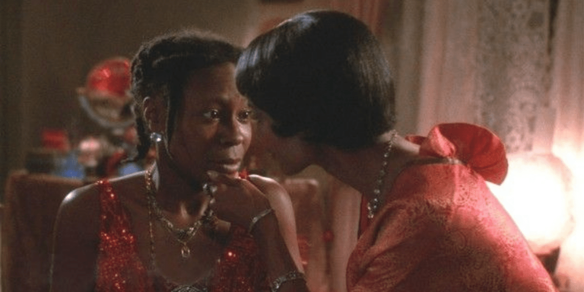 Shug has her fingers resting on Celie's chin, lifting her face upwards gently while Celie curiously stares at her.