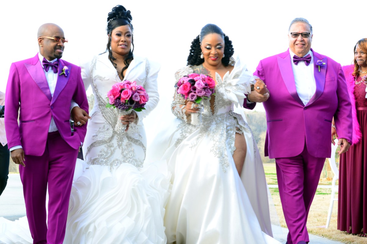 Da Brat & Jesseca “Judy” Dupart walk down he aisle in matching dresses and up do's. It is sunny in an outdoor wedding and they have matching pink and purple flower bouquets. Da Brat is escorted by Jermaine Dupre in a purple tuxedo.