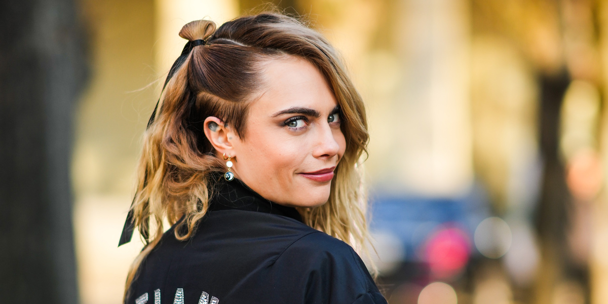 Cara Delevingne, a blonde woman with an undercut, smirks at the camera.