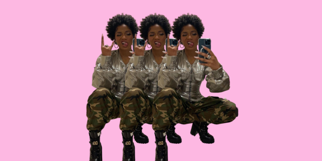 Keke Palmer taking a mirror selfie while sticking her tongue out and squatting, wearing a metallic silver top and camo pants with heeled boots