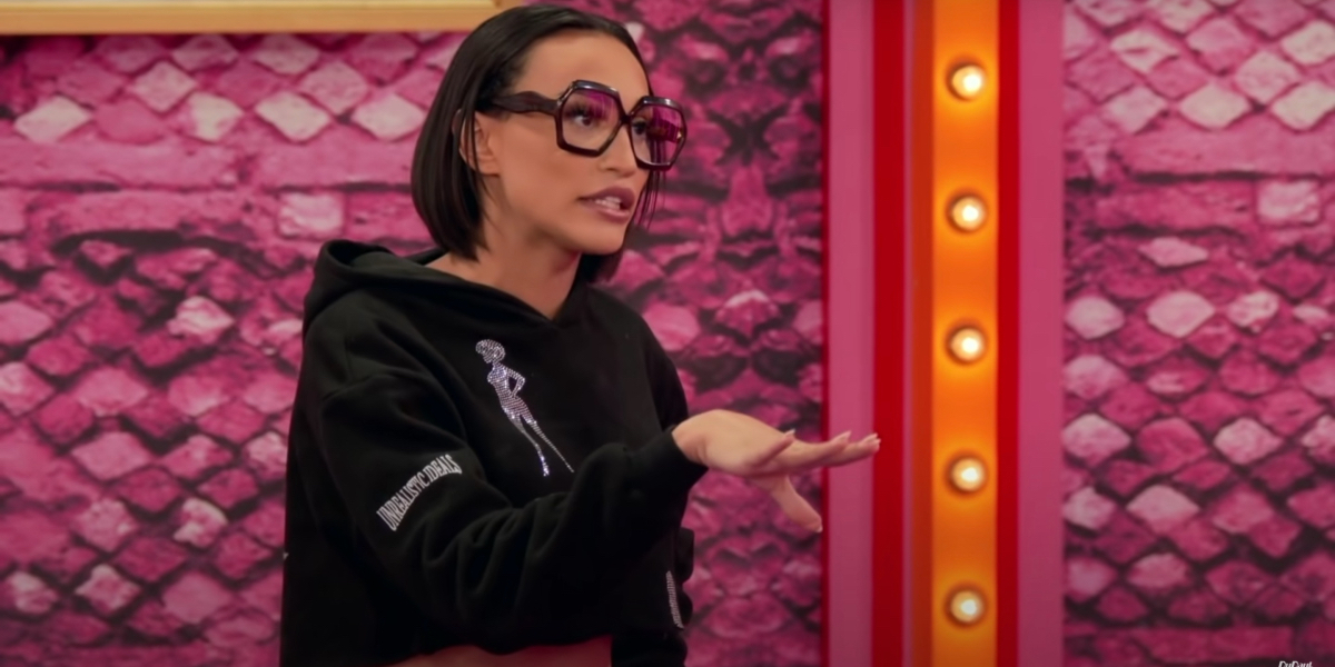 drag race recap 1408: Kerri Colby during the reading challenge wearing big fake glasses and a crop top sweatshirt.