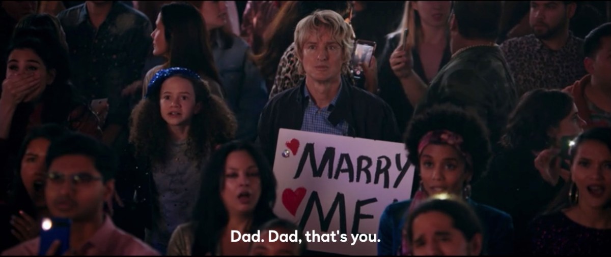 Charlie holds his Marry Me sign while his daughter is like, "Dad that's you"