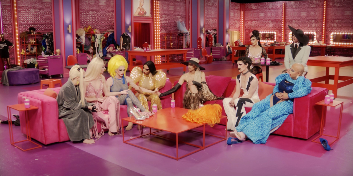 drag race recap 1407: During Untucked, Jasmine Kennedie sits between Bosco and Angeria. Bosco has a hand on her knee and Jasmine is reaching over to hold Kerri's hand on the other couch.