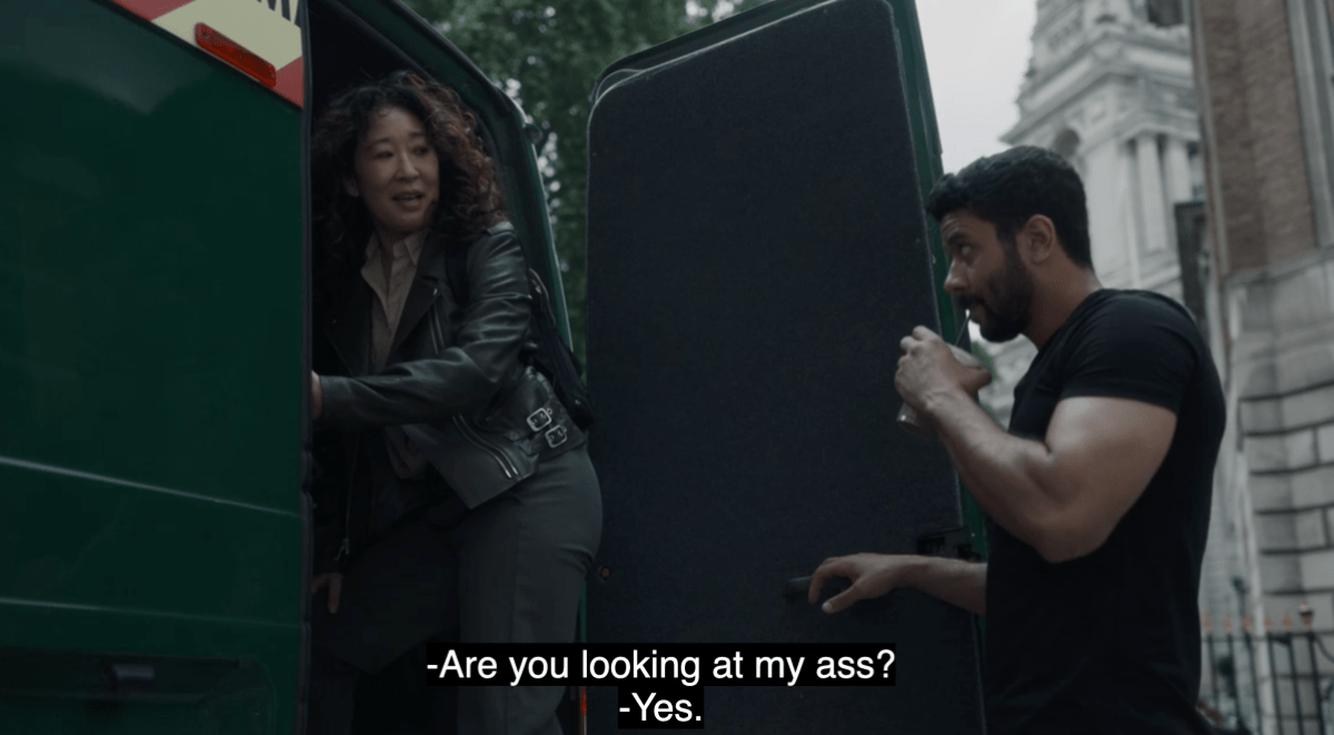 Eve (Sandra Oh) of Killing Eve wears a black moto jacket while getting into a van and turning back to look at Yusef, a man drinking a protein shake. Eve asks: Are you looking at my ass? Yusef says yes.