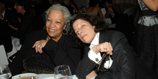 Toni Morrison and Fran Lebowitz lean in close together and smile for the camera at a black tie affair. Toni is in a black gown and fran is in a black suit coat with a white dress shirt.