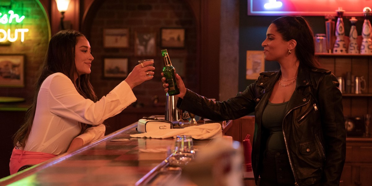 Dollface Season 2 screenshot: Stella (Shay Mitchell) and Liv (Lilly Singh) clink glasses over a bar