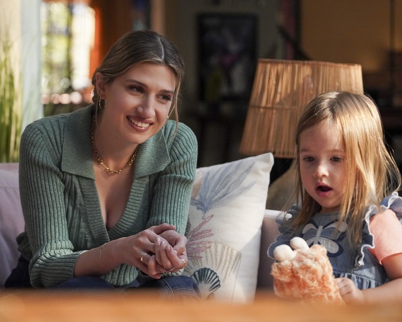 Nomi, wearing a green sweater, looks on as her daughter plays.