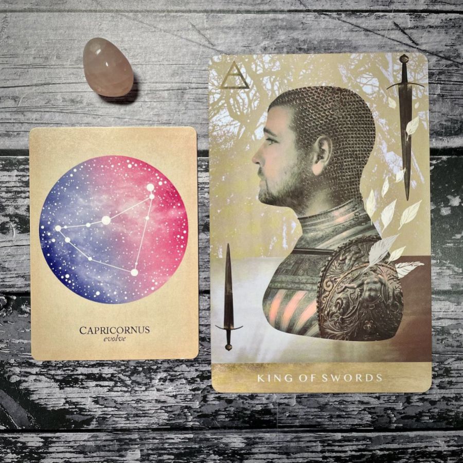 A card says Capricornus: evolve with a purple and pink circle, next to a card that says king of swords with an illustration of man in a knight’s uniform looking off to the left