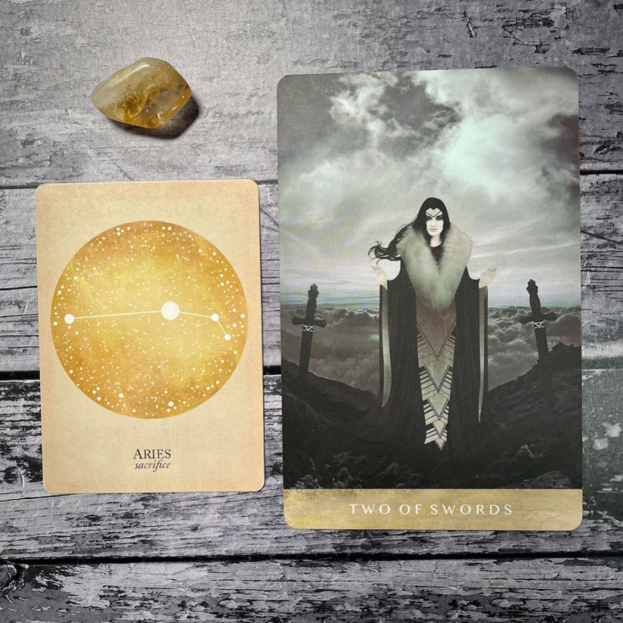 one card says Aries: Sacrfice in a gold circle, next to it a card for two of swords with a witch holding swords