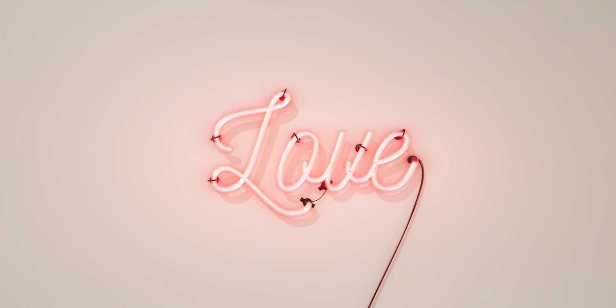 Neon sign that says the word Love in light pink, on a white concrete wall background