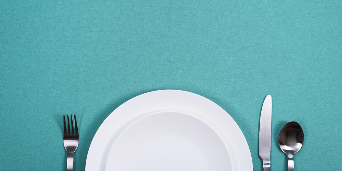 A fork, an empty white plate, a knife and a spoon are against a teal background.