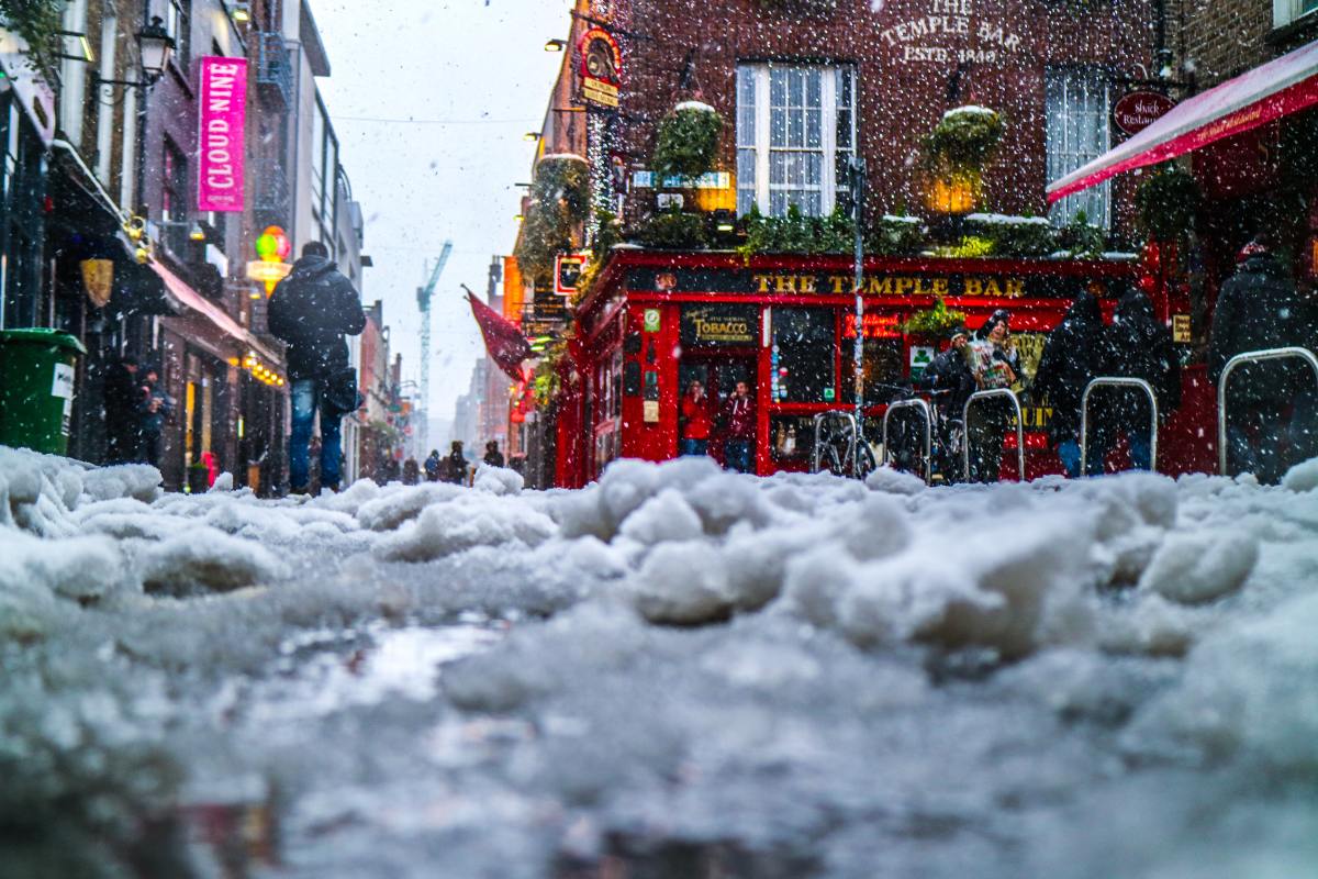 A snowy side street in dublin with a irish pub in the background.