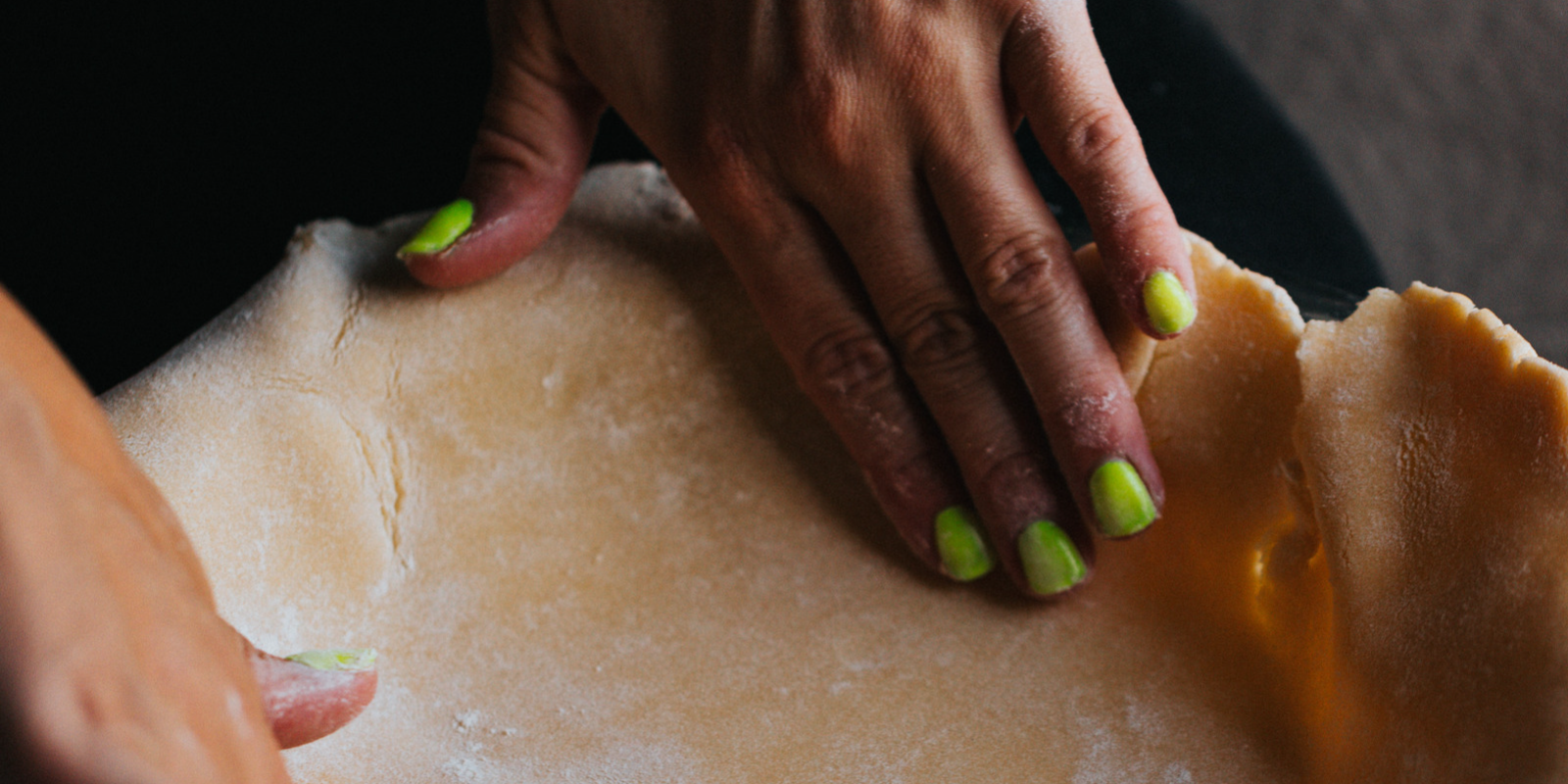 A manicured pair of hands forms a pie crusts into a baking tin.