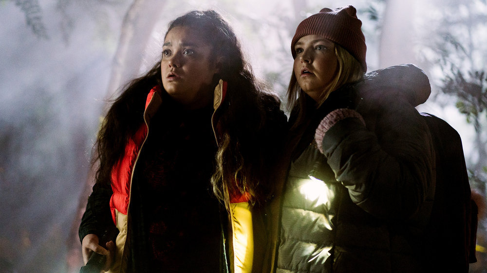 Press still of Astrid and Lilly bundled up and looking spooked in the woods