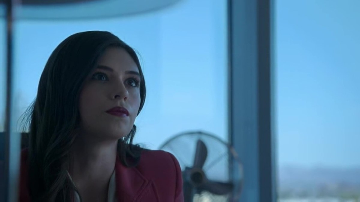 A shot of Liza, staring at Marina, who is off-screen. Liza is seated at her desk with a fan and the windows to an expansive view behind her.