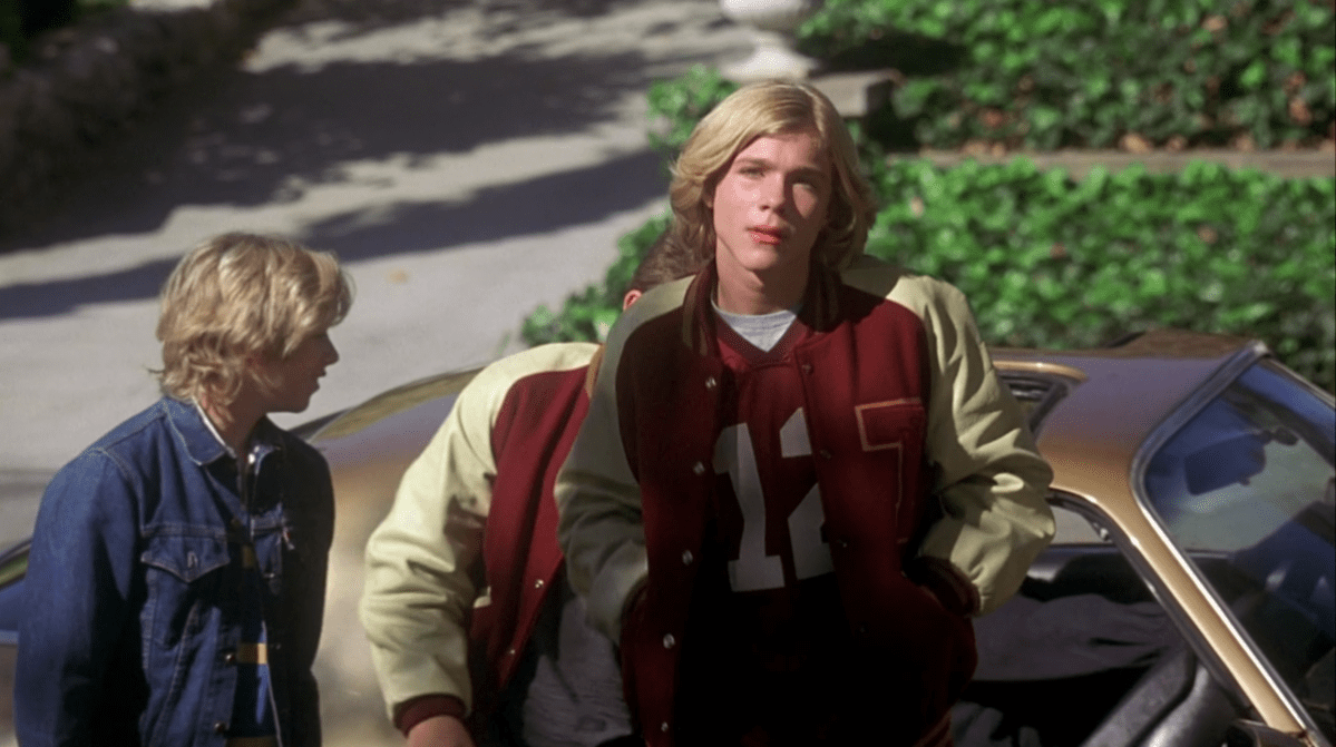 A group of teen boys with floppy hair and varsity jackets get out of a car