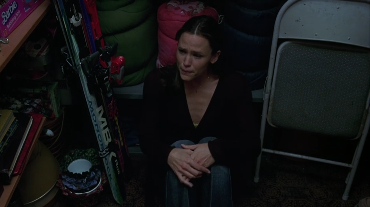 Jenna is sitting in a closet surrounded by old things from her childhood, looking distressed