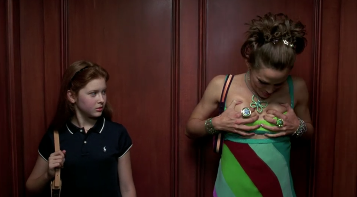 Jenna is wearing a colorblocked minidress and grabbing her boobs while a young girl stands in the elevator next to her looking embarrassed