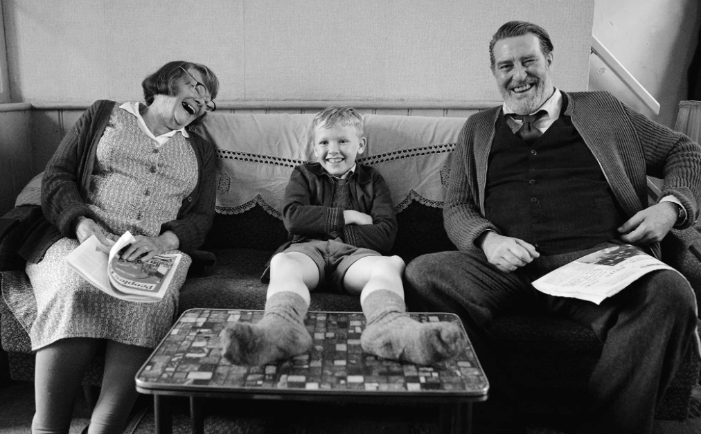 screenshot from Belfast of three white people on a couch laughing, a little boy in the middle