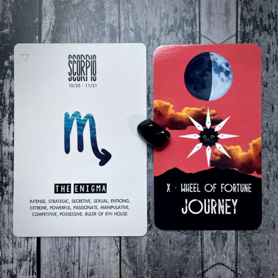 The Wheel of Fortune Journey card is orange with a moon in half eclipse and a star in from of orange clouds, next to it is a card that says Scorpio is The Enigma