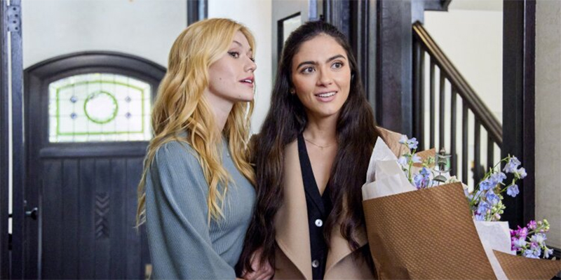 Arienne Mandi and Katherine McNamara stand in a doorway holding flowers in Hallmark's "Love, Classified"