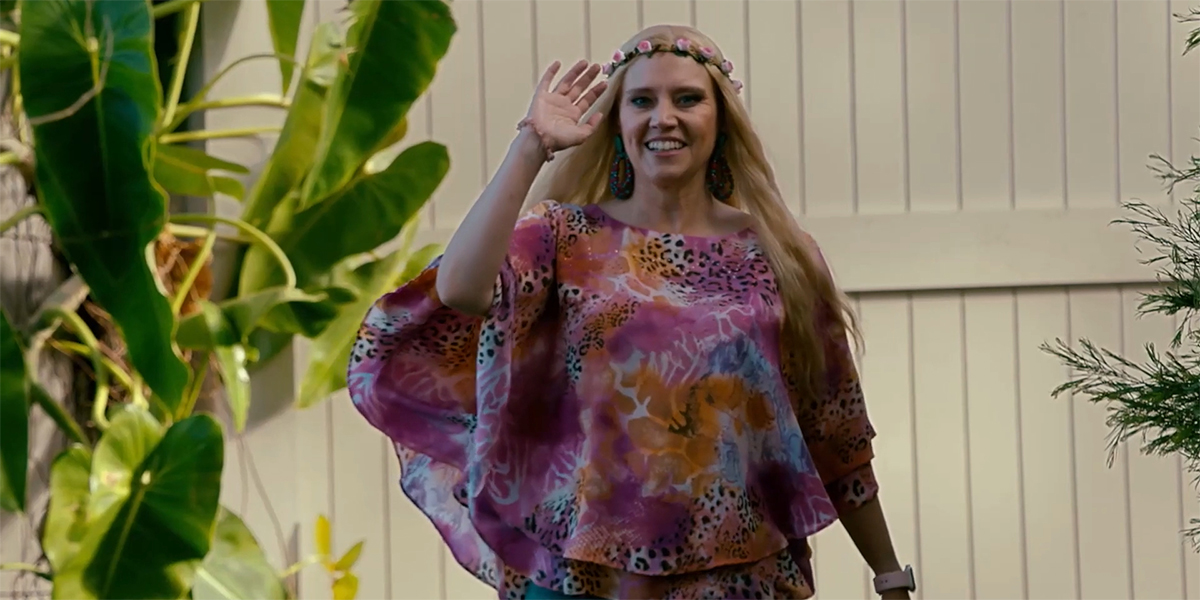 Kate McKinnon as Carole Baskin in a pink leopard print shirt, waving