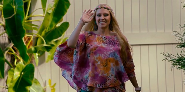 Kate McKinnon as Carole Baskin in a pink leopard print shirt, waving