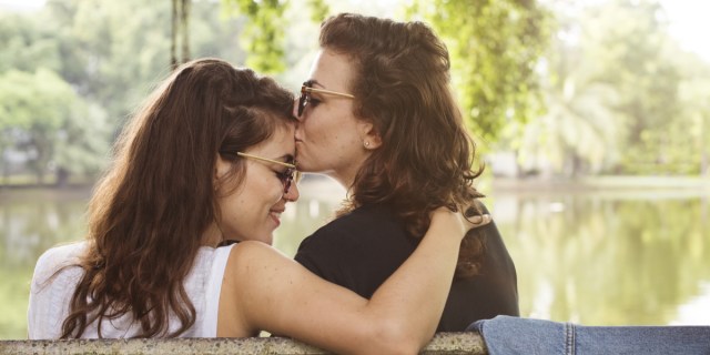 two women on a bench, one is 15 years old than the other and kissing her forehead, they are clearly happy and in love