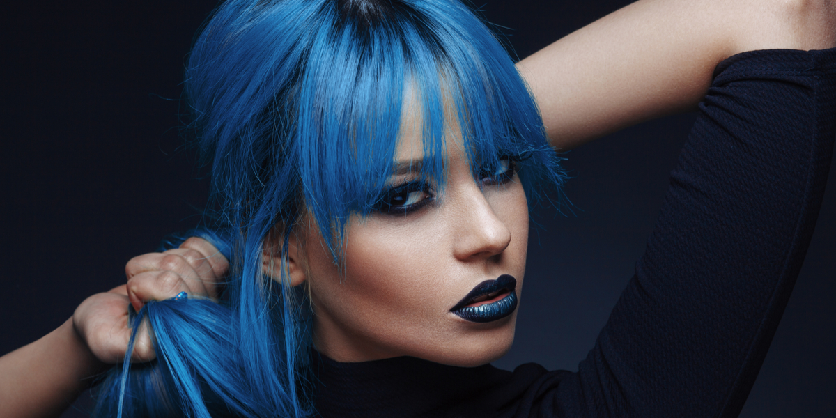 A woman with blue hair and blue lipstick against a black backdrop