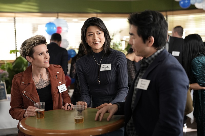 Greta and Katherine gather around a cocktail table at their high school reunion and reminisce with Randy Kwan.