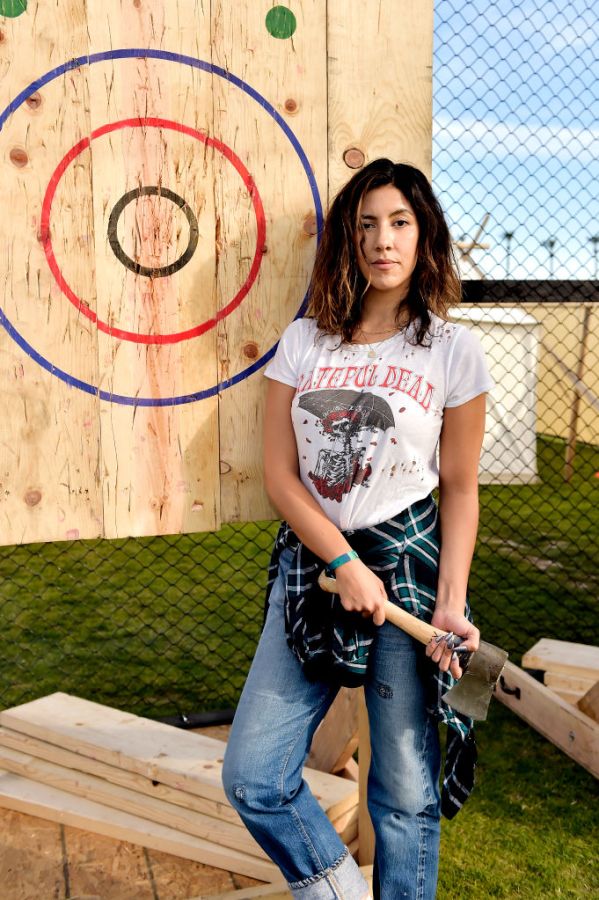 Stephanie Beatriz holds an axe while wearing a Grateful Dead shirt, flannel, and jeans