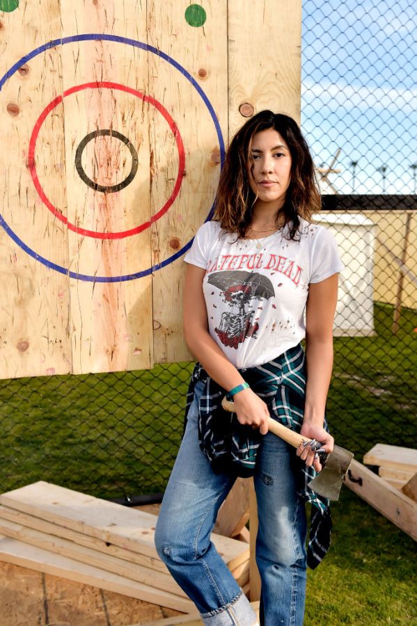 Stephanie Beatriz holds an axe while wearing a Grateful Dead shirt, flannel, and jeans