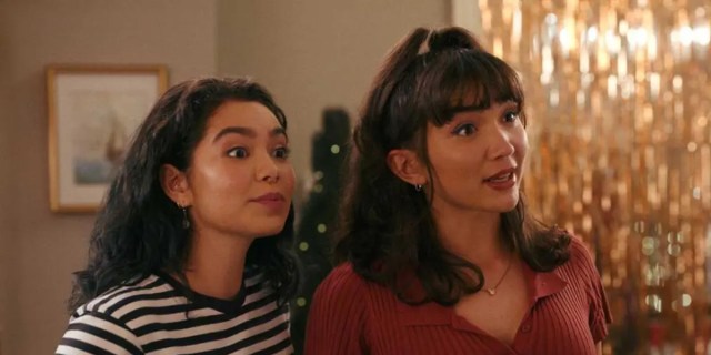 In a still from Hulu's Crush, Rowan Blanchard and Auliʻi Cravalho make a silly face together at the right of camera. Auli'i is in a striped shirt and Rowan is in a red shirt with her hair in a messy updo. There are gold streamers hanging behind them.