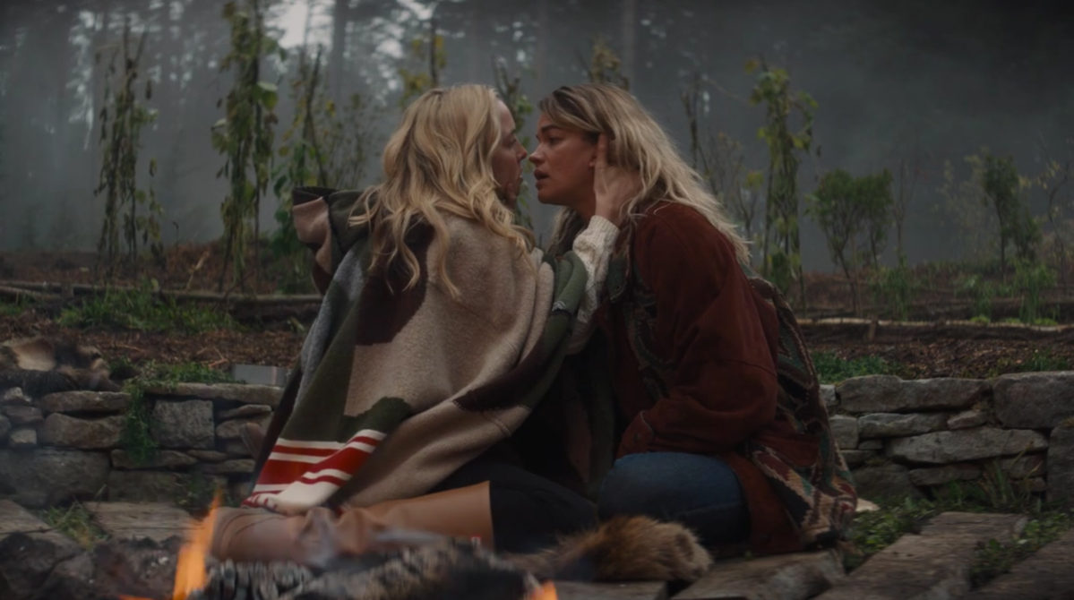 Villanelle and Gunn are sitting by a fire, draped in thick wool coats on Killing Eve. Villanelle holds Gunn by the neck.