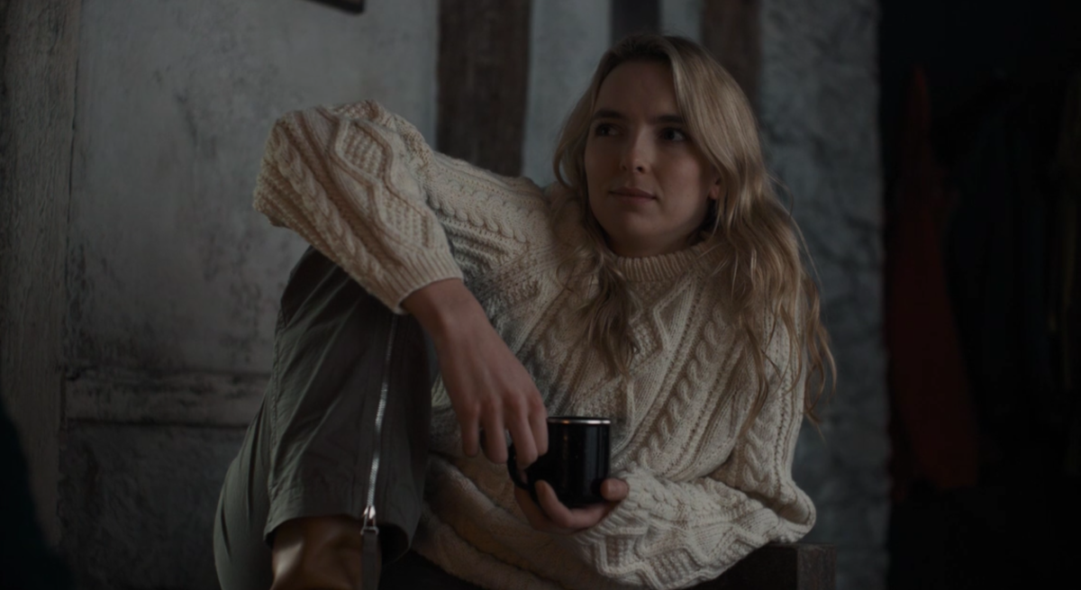 Villanelle wears a fisherman sweater and holds a mug while looking at a straight couple skeptically in the Killing Eve series finale