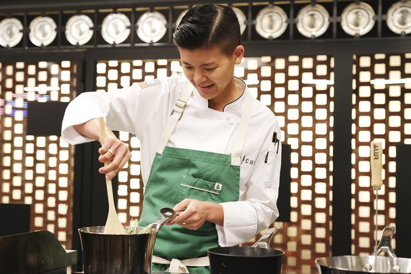 Wearing a green apron, Jo stirs her pot with a wooden spoon during the elimination challenge.