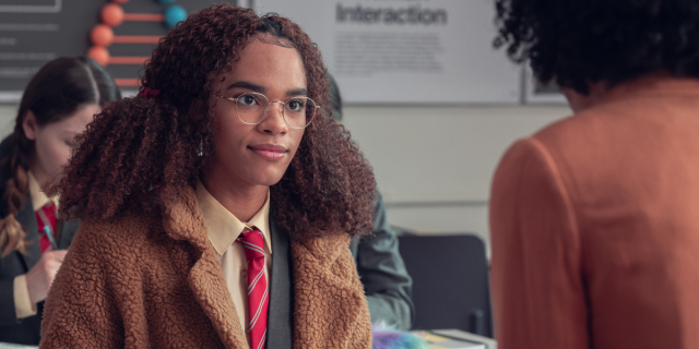 Yasmin Finney as Elle Argent wears a school uniform and glasses while in a classroom.
