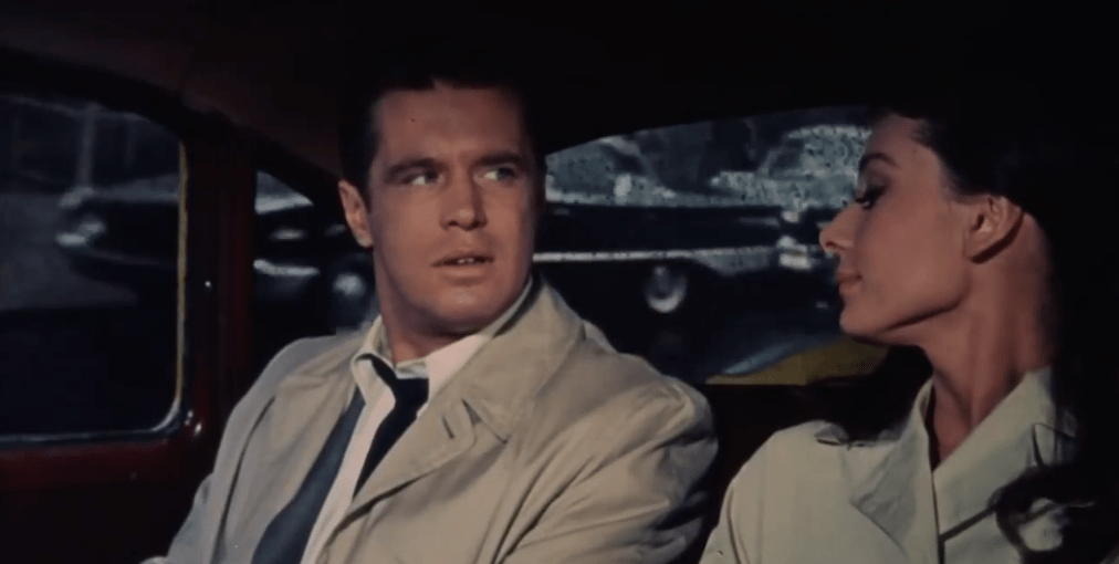George Peppard is wearing a trenchcoat and sitting next to Audrey Hepburn in a car in Breakfast At Tiffany's