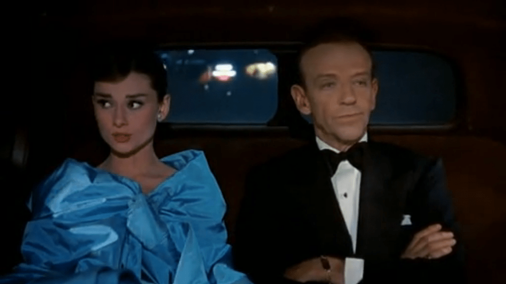 In Funny Face, Audrey Hepburn and Fred Astaire sit in the back of a car. Audrey is wearing a poofy blue dress, and Fred is wearing a suit with bowtie.