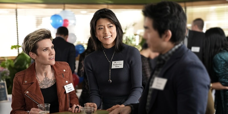 Greta and Katherine gather around a cocktail table at their high school reunion and reminisce with Randy Kwan.