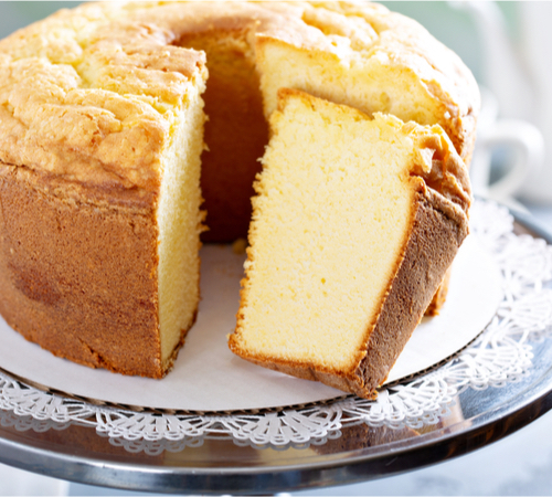 A donut-shaped loaf of yellow pound cake is on a glass plate with a lace pattern on the edges.