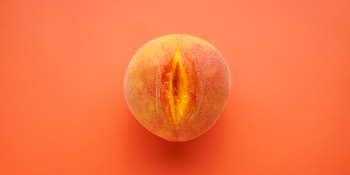 Against an orange background, there is a peach with a slit cut down its center, causing the fruit to resemble a vulva.